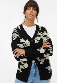 Cardigan noir avec motif floral blanc, col en V, manches longues et fermeture à boutons ; en tissu tricoté doux, idéal pour les superpositions.