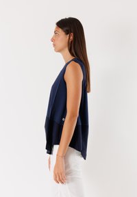 Top senza maniche blu navy con un design a strati, caratterizzato da un collo rotondo e un orlo posteriore leggermente più lungo. Realizzato in tessuto morbido.