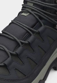 Κοντινό πλάνο ενός σκουρόχρωμου γκρίζου μποτάκιου πεζοπορίας με παχιά πάνελ από ύφασμα, ενισχυμένες εγκάρσιες ραφές σε ζιγκ ζαγκ και στρογγυλά κορδόνια με σχέδιο.