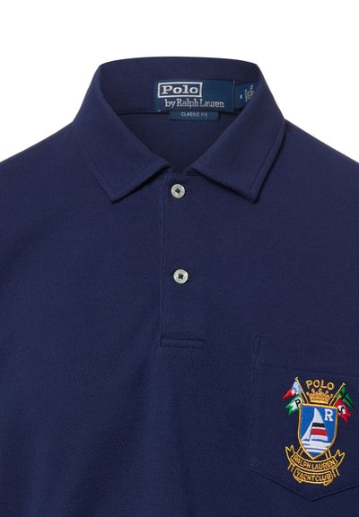 Polo bleu marine avec étiquette coupe classique, deux boutons blancs, et blason brodé Polo Ralph Lauren Yacht Club sur la poche poitrine.