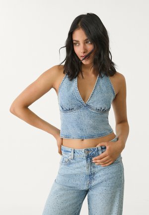 Denim-Halter-Crop-Top mit V-Ausschnitt und strukturiertem, hellblauem Stoff, kombiniert mit hoch taillierten, passenden Jeans mit dezenten Verzierungen.