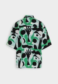 Chemise à manches courtes arborant un motif géométrique en vert, noir et blanc, avec diverses formes abstraites et motifs de mains sur un tissu léger.