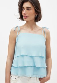 Hele sinine kihtide top, millel on plekitud disain, reguleeritavate õlavarrepaelte ja sirge kaelusega. Valmistatud pehmest ja kergest kangast.