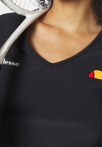 Svart sportstopp med V-ringning, med en vit logotyp och en flerfärgad accentdesign i röd, gul och orange. Slät textur.