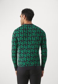 Maglione verde e nero con motivo a lettere ripetute, collo rotondo e maniche lunghe, con un orlo texturizzato blu navy.