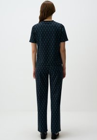Set di pigiama nero e blu con maniche corte, vestibilità ampia e design geometrici che presentano diamanti e frecce. Texture liscia.