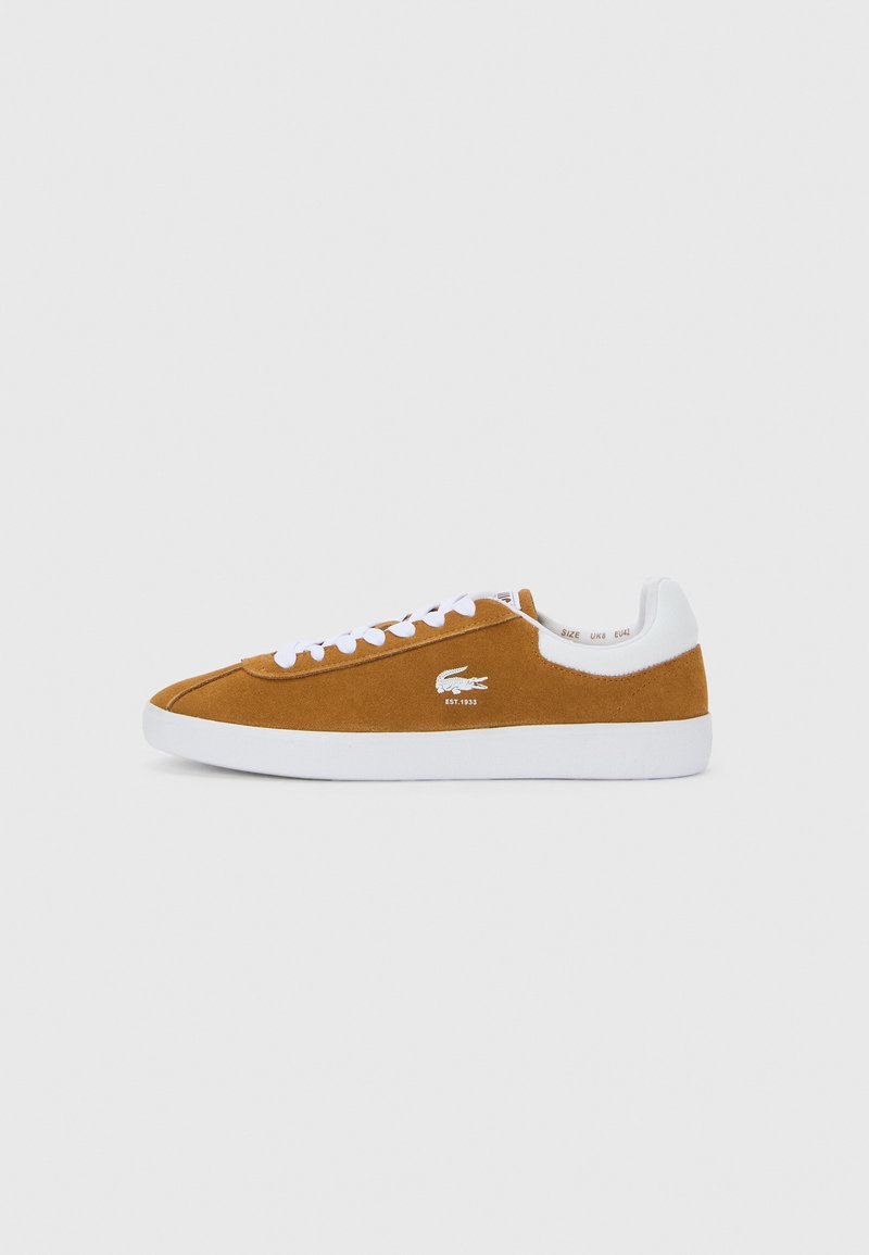 Καφέ σουέτ χαμηλά αθλητικά παπούτσια με λευκές κορδόνες, λευκή σόλα και λευκό γιακά στη φτέρνα, με ένα μικρό λογότυπο κροκόδειλου στη πλευρά.