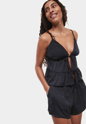 Zwarte, lichtgewicht, mouwloze peplumtop met een cinched taille en verstelbaar strikdetail, gecombineerd met bijpassende shorts met zakken.
