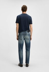 T-shirt blu navy a girocollo abbinato a jeans in denim blu medio. I jeans sono leggermente rovinati, con una vestibilità affusolata e tasche posteriori visibili.