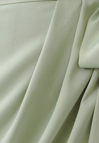 Svetlozeleno blago z gladko teksturo, ki vključuje drapirane gube in mehke linije. Material se zdi lahek in zračen.