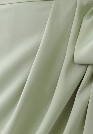 Lichtgroene stof met een gladde textuur, gekenmerkt door gedrapeerde plooien en zachte lijnen. Het materiaal lijkt licht en vloeiend.