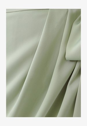 Lichtgroene stof met een gladde textuur, gekenmerkt door gedrapeerde plooien en zachte lijnen. Het materiaal lijkt licht en vloeiend.