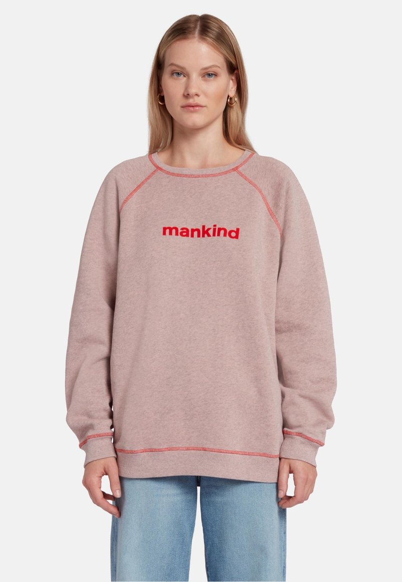 Sweatshirt en polaire rose avec des coutures rouges, portant le mot "mankind" en lettres rouges en gras sur la poitrine. Coupe décontractée.