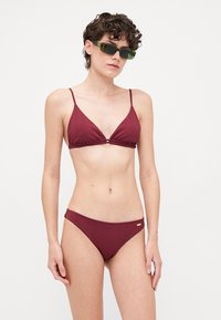 Maroon bikini set with a ribbed texture. Triangular top with thin straps, matching low-rise briefs. Gold accent detail on the briefs.