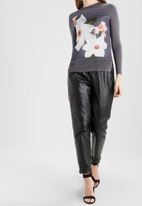 Grå långärmad topp med blommönster, i kombination med svarta läderbyxor. Toppen har en figurnära silhuett och rund halsringning.