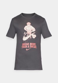 Mørkegrå bomulls-T-skjorte med grafisk design i lyserosa, med teksten "BREAK MORE THAN A SWEAT" og Nike-logoen nederst.