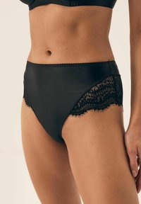 Czarne majtki wysokiego stanu wykonane z gładkiego materiału z koronkowymi akcentami po bokach, charakteryzujące się falbaniastymi brzegami i bezszwowym krojem.