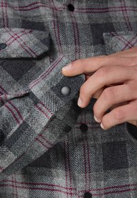 Cămașă din flanel cu carouri gri, având un model de tip herringbone, accente roșii și bleumarin, cu manșete cu nasturi și nasturi negri.