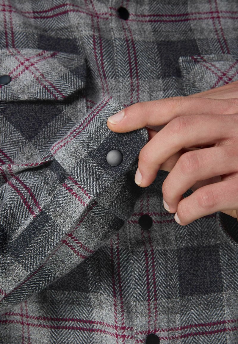 Cămașă din flanel cu carouri gri, având un model de tip herringbone, accente roșii și bleumarin, cu manșete cu nasturi și nasturi negri.