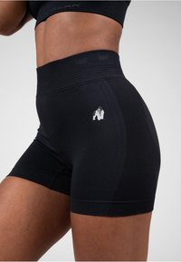 Zwarte hoge sportshorts met een gestructureerde tailleband, voorzien van een wit grafisch logo aan de linkerkant en een aansluitend ontwerp.