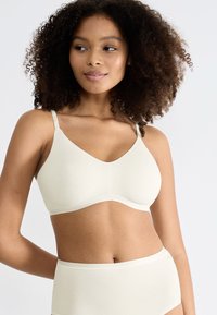 Reggiseno wireless beige chiaro con una texture liscia e elastica, dotato di scollatura a V, spalline regolabili e un design semplice e senza cuciture.