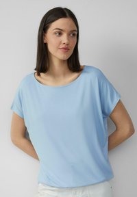 Lichtblauw T-shirt met korte mouwen, een ruime halslijn, zachte textuur en een relaxte pasvorm. Gladde stof met minimale detailing.