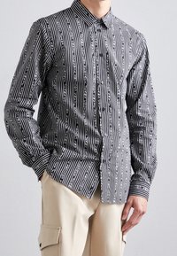 Camicia a maniche lunghe bianca e nera con righe verticali e motivi testuali. Realizzata in tessuto liscio, con colletto e polsini abbottonati.