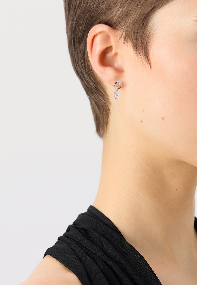 Srebrni obročasti uhani, ki vsebujejo majhen prozoren dragulj in listnato kapljico kot dodatek, poudarjajo eleganten in sodoben dizajn.