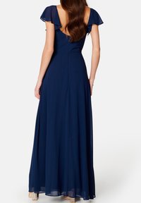 Robe longue bleu marine avec des manches courtes en tulle volantées et un dos décolleté. Le tissu fluide tombe jusqu'au sol avec une légère silhouette en A.