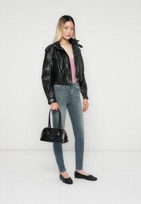 Sort læder cropped jakke med trykknapskrave, lys pink top, blå skinny jeans, sort håndtaske og sorte flade sko med sløjfedetalje.