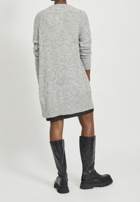 Grå strikket cardigan med lange ærmer, knælang. Kombineret med slanke sorte læderstøvler til knæet med kraftige såler.