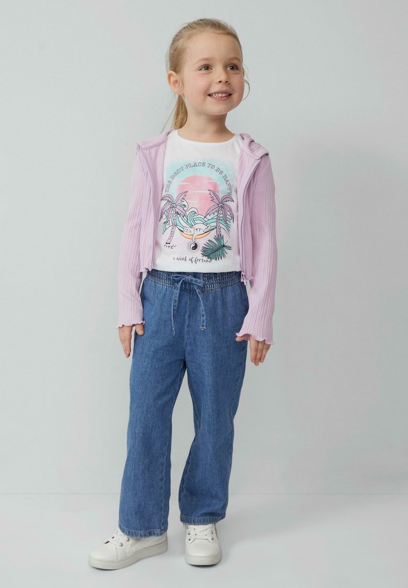 Helllila Zip-Up Hoodie über einem weißen T-Shirt mit einem Palmbaum-Design, kombiniert mit blauen Jeans und weißen Sneakern.