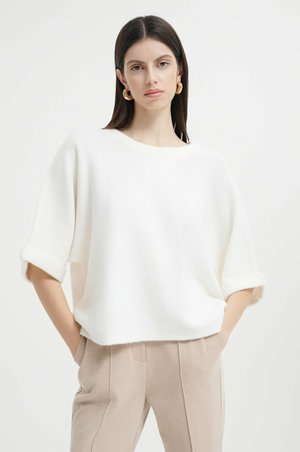 Maglione bianco, ampio e comodo, realizzato in materiale morbido e texturizzato, con maniche corte arrotolate, abbinato a pantaloni beigi. Design semplice e pulito.