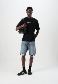 Camiseta negra de manga corta con "atelier dept." impreso en dorado, pantalones cortos de mezclilla desgastados, bolso negro y zapatillas negras con detalles blancos.