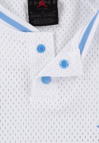 White mesh polo shirt with blue buttons and accents, featuring a collar and a tag indicating size and brand. Textured pattern with ventilation holes.