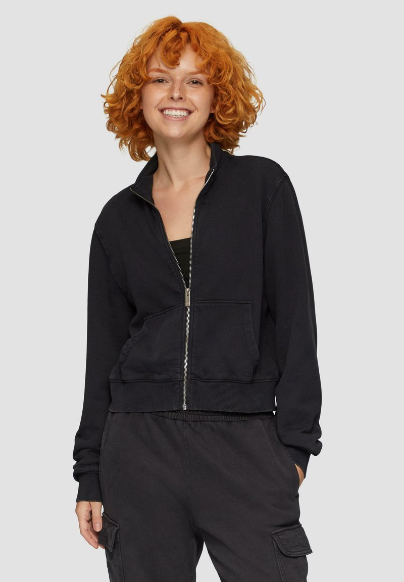 Czarna bluza zapinana na zamek z ribbowymi mankietami i paskiem w talii, z przednią kieszenią i wysokim kołnierzem, wykonana z miękkiego materiału.