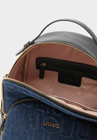 Ronde rugzak van zwart leer met denim accenten, gouden rits en een roze binnenkant. Beschikt over een ritsvak en een merkembleem aan de binnenkant.