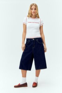 Balta marškinėliai su raudonais akcentais ir užrašu "HARD TO PLEASE", derinami su tamsiai mėlynais džinsiniais kulotais ir rudos spalvos loferiais su raudonais akcentais.