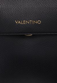 Bolso de cuero negro con una superficie texturizada, logo dorado "VALENTINO" y un cierre de solapa elegante con un sutil detalle de acento.