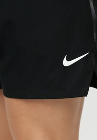 Κοντινό πλάνο ενός ατόμου που φοράει μαύρα αθλητικά σορτς με λευκό λογότυπο Nike στο αριστερό μηρό.