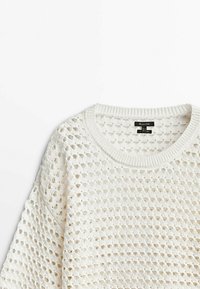 Valkoinen neulepusero, jossa on löysä ja avoin kudontakuvio. Pyöreä pääntie ja ribbauskankaiset hihansuut. Pehmeä rakenne, rento muotoilu.