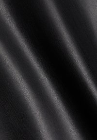 Surface en cuir noir texturé avec des plis doux en forme de vague créant des reflets et des ombres sur le matériau.