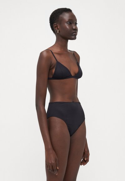 Melnā bikini, kas sastāv no trijstūra krūštura un augstām biksēm. Gluda auduma ar plāniem siksnām un minimālām šuvēm.