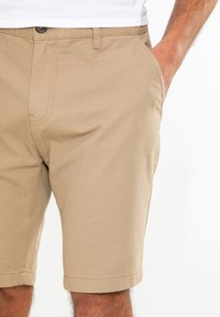 Shorts beiges en tissu mélangé coton. Avec un devant plat, deux poches latérales et un ourlet propre. Design classique avec une texture subtile.