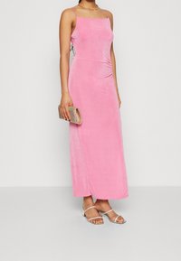 Różowa maxi sukienka bez rękawów o gładkiej fakturze, z bocznymi marszczeniami, w połączeniu z sandałami na obcasie w kolorze srebrnym i irydyscencyjną kopertówką.