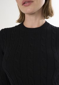 Pull en tricot noir avec un col rond côtelé, un motif en relief de câble et une silhouette près du corps. Tissu doux avec une finition lisse.