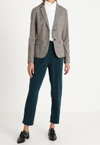 Šedý kostkovaný blazer se dvěma předními kapsami, kombinovaný s tyrkysovými kalhotami a černými botami. Blazer má klopový límec a zapínání na knoflík.