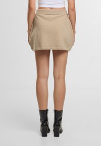 Pletená béžová minisukně se širokým páskem, jemnou texturou a rozšířeným střihem. K tomu černé kotníkové boty se čtvercovými podpatky.
