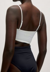Witte crop top met dunne bandjes, met een slank ontwerp, gecombineerd met zwarte high-waisted onderstukken, die gladde stof en strakke lijnen laten zien.