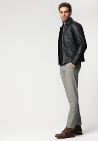 Czarna skórzana kurtka z kołnierzem zestawiona z szarymi spodniami w kratę i brązowymi butami na sznurówki. Strój charakteryzuje się dopasowanym krojem i gładką fakturą.